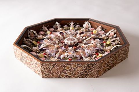 A side view of an octagonal shellwork shadowbox with intricate floral and geometric patterns made from shells, set inside a wooden frame with decorative inlays.